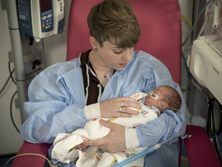 Woman sat in a hospital chair holding her baby in her arms while looking down tenderly
