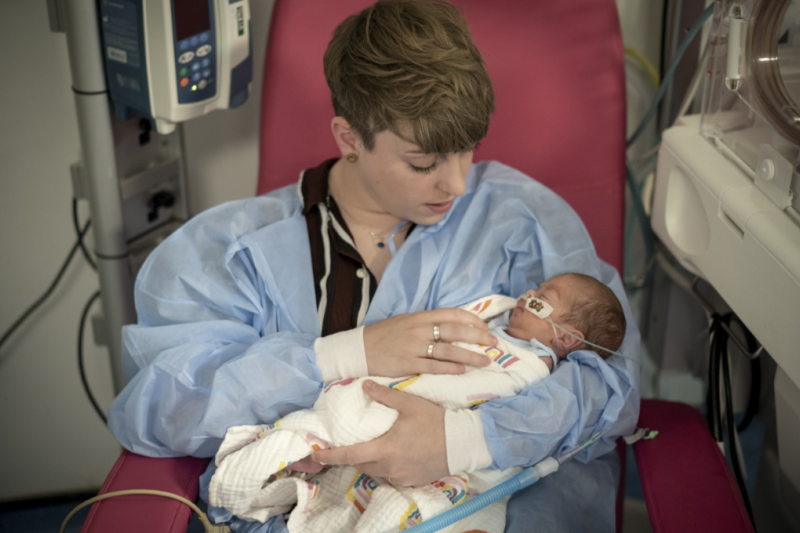 Woman sat in a hospital chair holding her baby in her arms while looking down tenderly