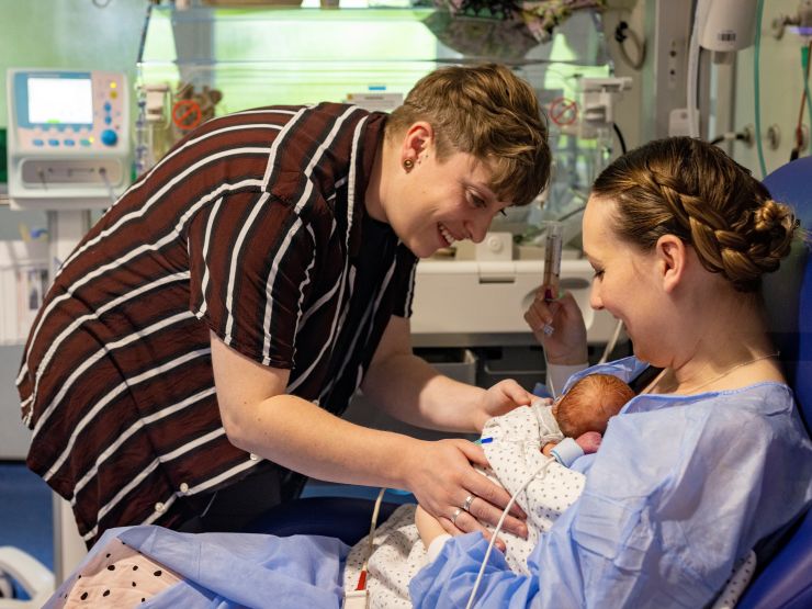 Woman holding baby on her chest in a hospital setting while her partner gently touches the baby's side