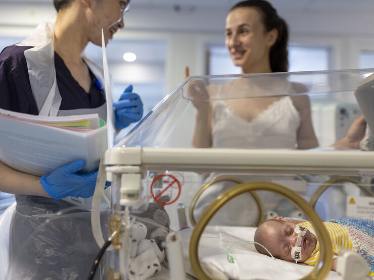 Mum and nurse talking in the background with a sleeping baby in an incubator in the foreground