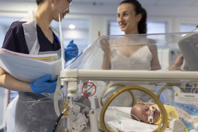 Mum and nurse talking in the background with a sleeping baby in an incubator in the foreground