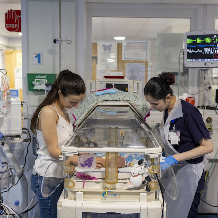 Mum and nurse standing over incubator looking at the baby