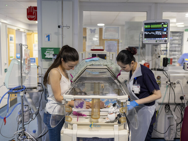 Mum and nurse standing over incubator looking at the baby