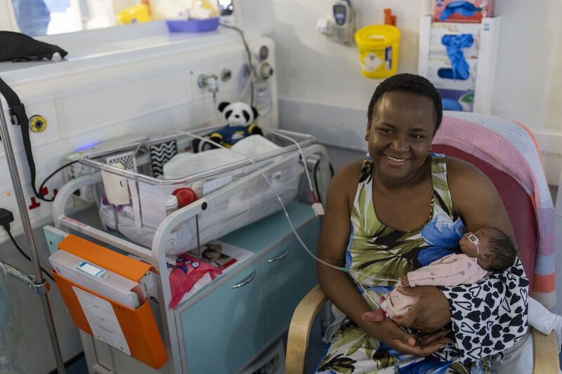 Mum smiling while holding her baby sat next to an incubator