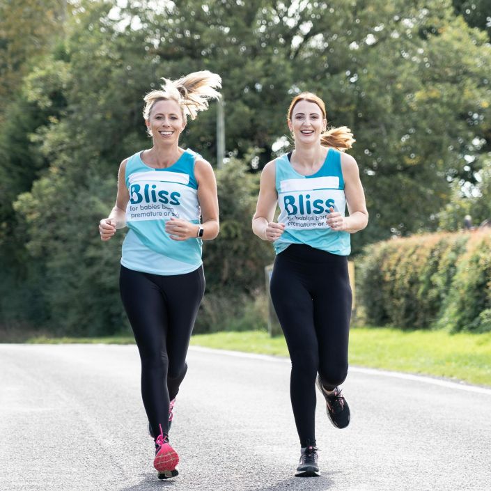 Two women running down the road together wearing Bliss running vests