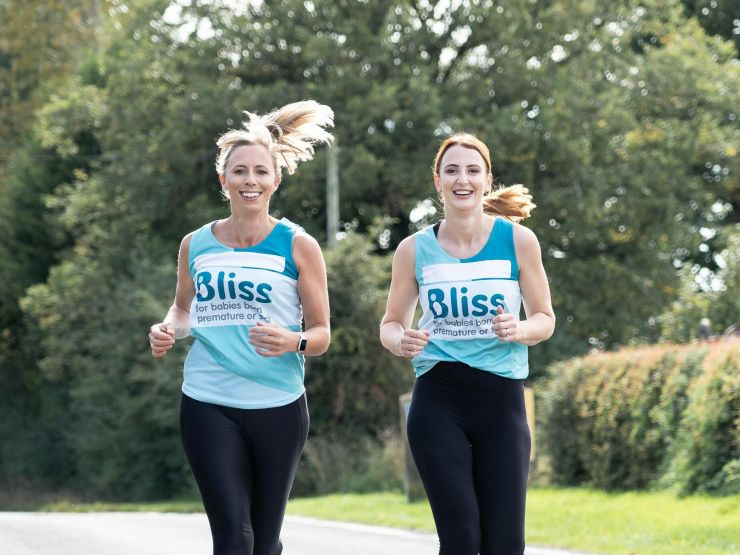 Two women running down the road together wearing Bliss running vests