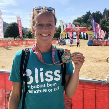 Lady in Bliss t-shirt holding her medal and smiling