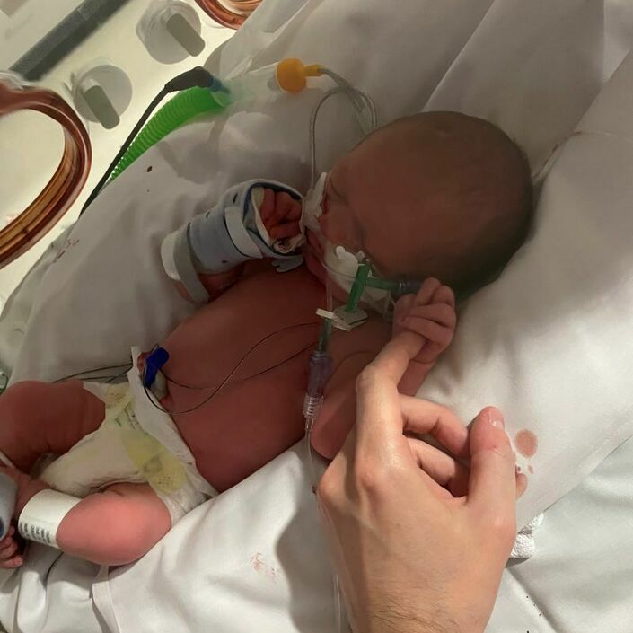 Baby in hospital attached to tubes holding parent's finger