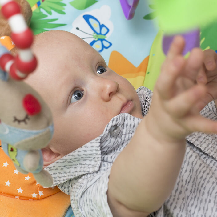Baby lying on his back reaching up for a toy