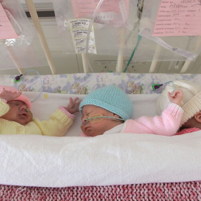 Triplets sleeping together in a cot attached to feeding tubes