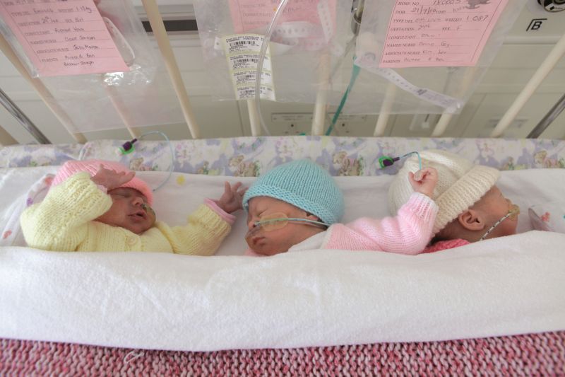 Triplets sleeping together in a cot attached to feeding tubes