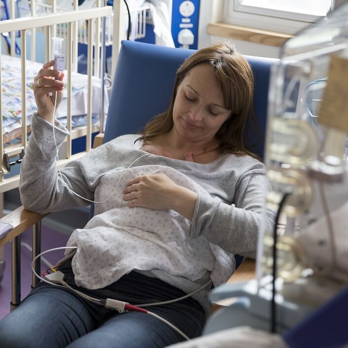 Mother in a hospital chair with her baby in her arms with tubes attached