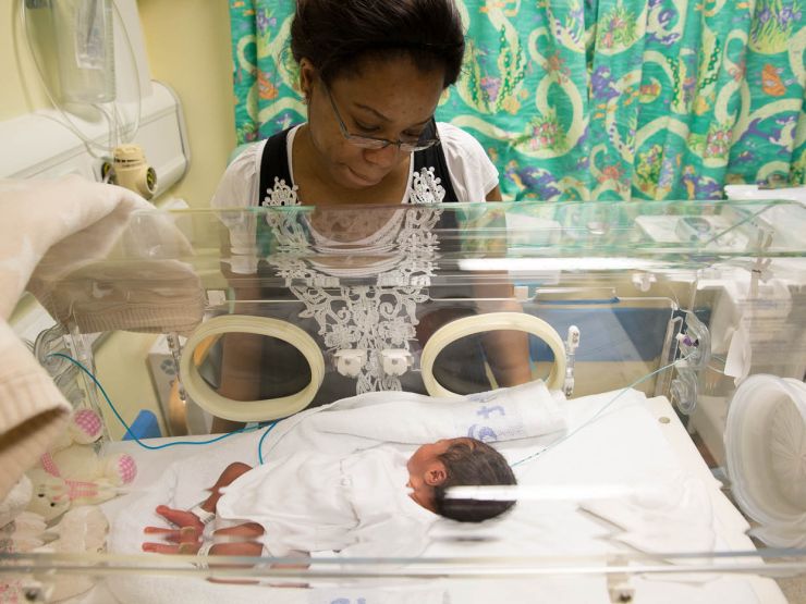 Mum in neonatal unit looking at her baby who is lying in a hospital cot