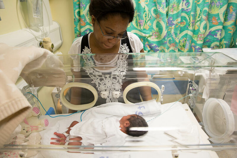 Mum in neonatal unit looking at her baby who is lying in a hospital cot