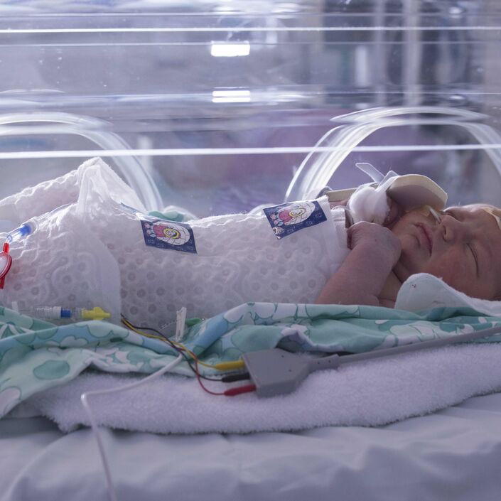 Baby in an incubator lying on a knitted blanket and wrapped in an insulated plastic layer