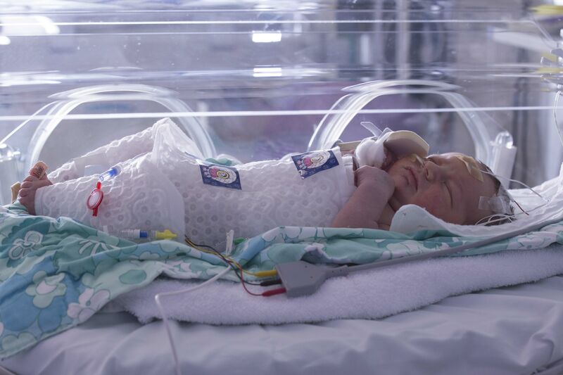 Baby in an incubator lying on a knitted blanket and wrapped in an insulated plastic layer