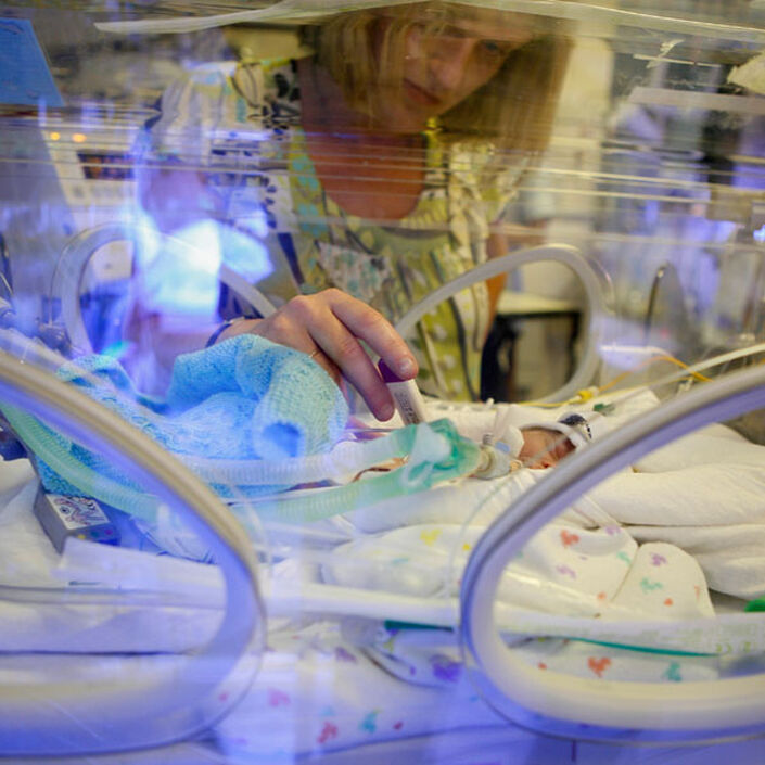 Mum touching her premature baby through an incubator