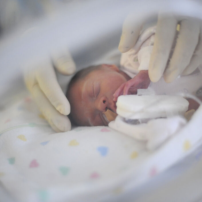 A baby in an incubator being gently touched by hands with latex gloves on