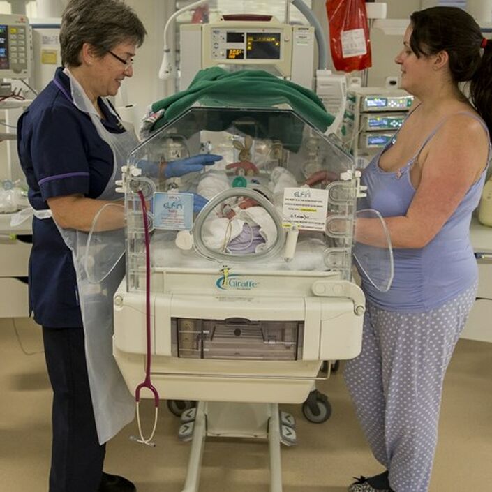 Mum and nurse with their hands through an incubator touching a baby