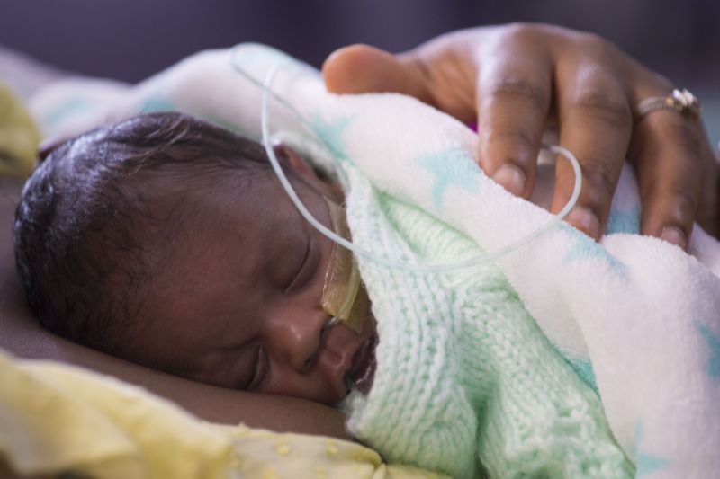 Premature baby wrapped in blanket sleeping on parent's chest with parent's hand on baby's back