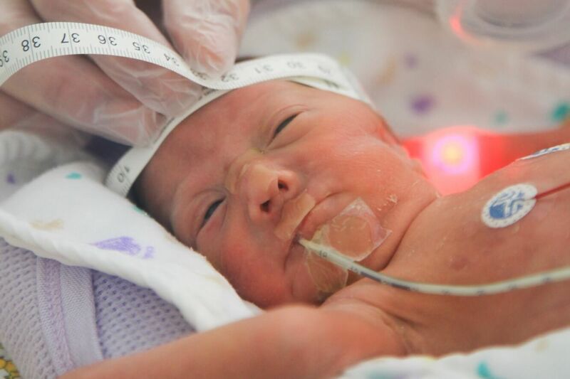 Baby in hospital having its head circumference measured by nurse in gloves