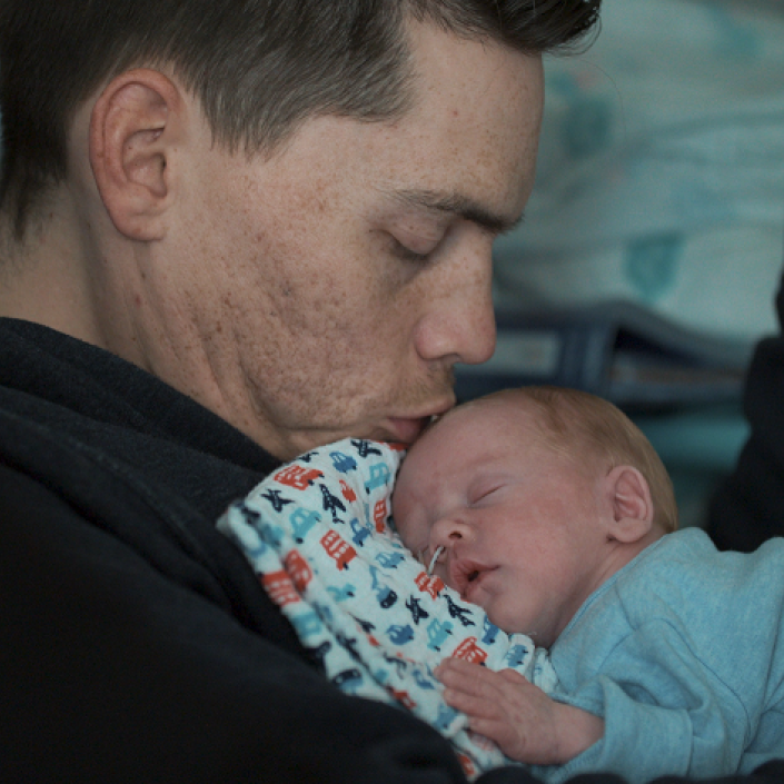 Dad holding his premature baby on his chest while he kisses baby's head