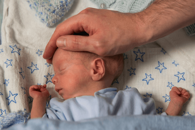 Parent placing hand on baby's head while baby sleeps peacefully