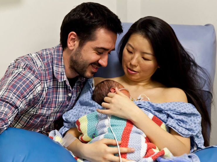 Mum and dad sat together with mum holding baby on her chest
