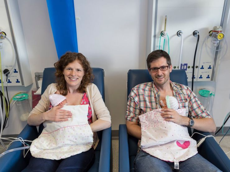 Mum and dad sat in hospital chairs smiling while holding twin babies