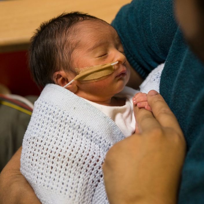 Dad holding baby wrapped in blanket attached to feeding tube