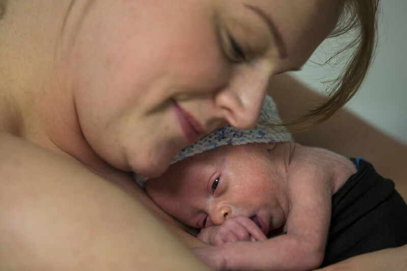 Baby cuddling on mum's chest skin to skin with mum leaning her head down towards baby and smiling