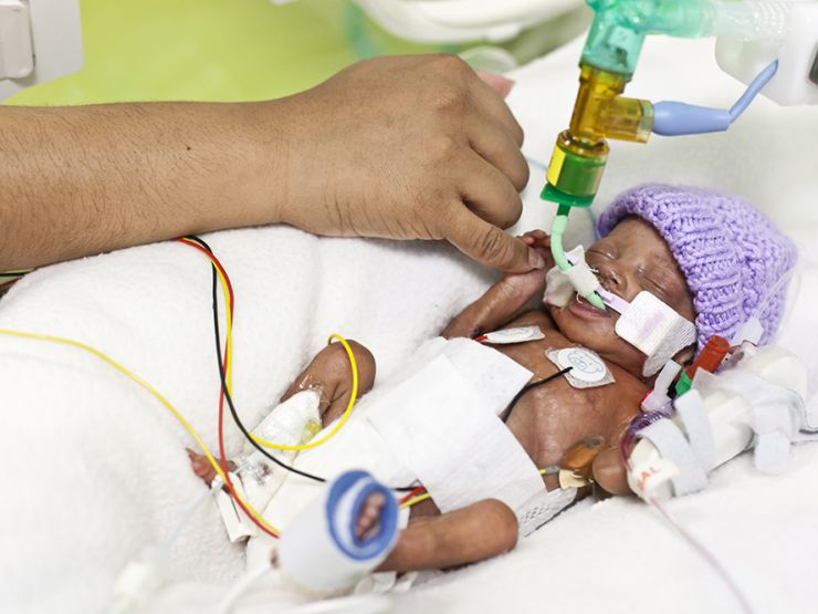 Baby in cot holding onto parent's finger