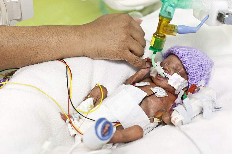 Baby in cot holding onto parent's finger
