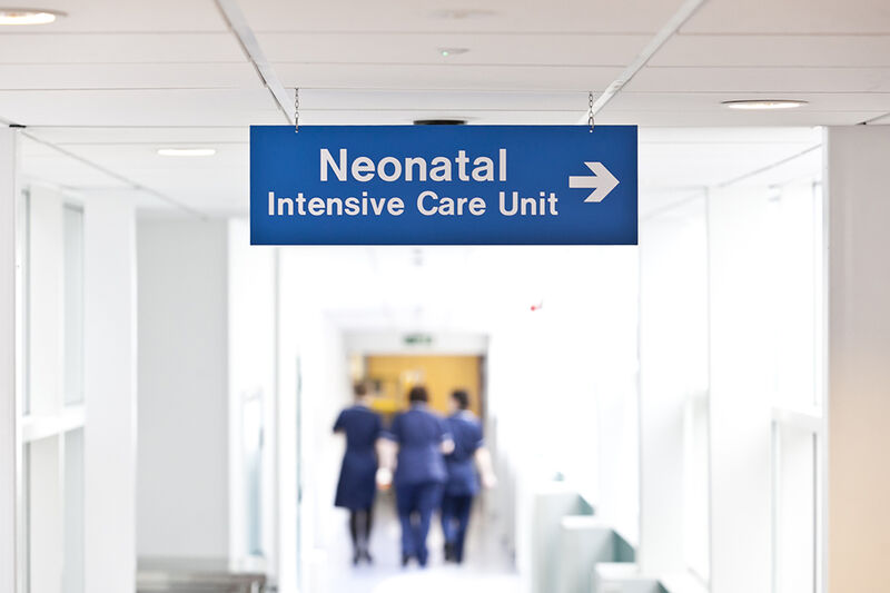 Hospital sign for neonatal intensive care unit with nurses blurred in background