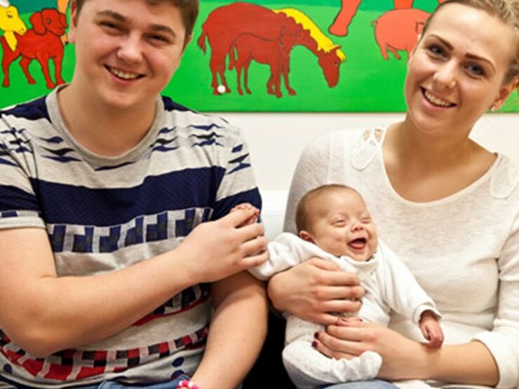 A couple with their baby smiling at camera about to go home