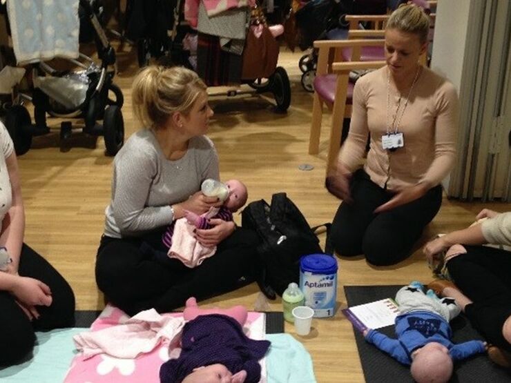 Group of mothers sat on the floor with two babies lying down while one baby being bottle fed