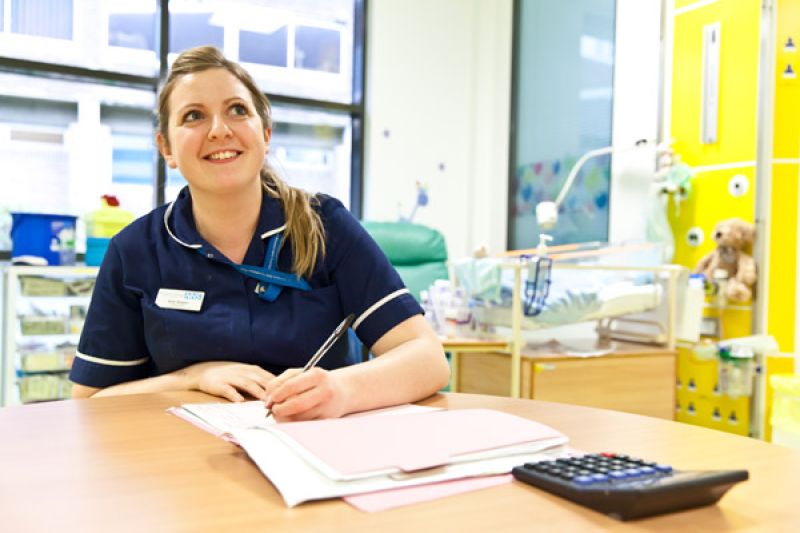 Nurse doing paperwork sitting at a desk looking up and smiling