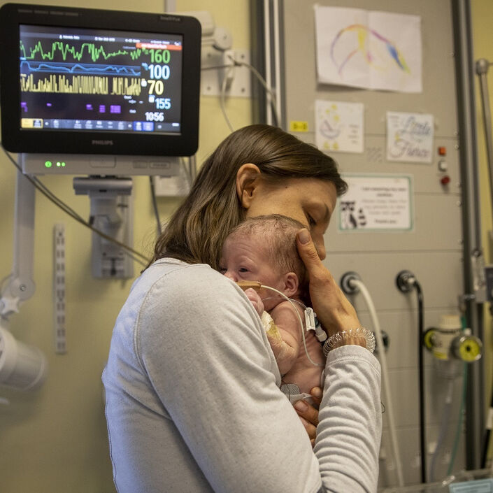 Mum standing up in unit holding baby close to her on one shoulder with baby looking over shoulder and mum's hand on baby's head