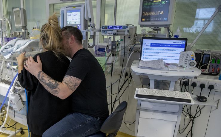 Mum And Dad At Incubator With Backs To Camera And Dads Arm Around Mum