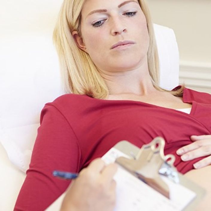 Pregnant woman on hospital bed, with her pregnant belly showing, with midwife writing notes