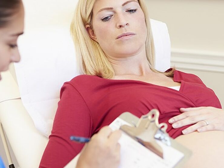 Pregnant woman on hospital bed, with her pregnant belly showing, with midwife writing notes