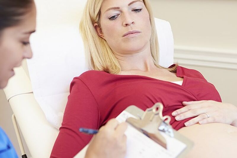 Pregnant woman on hospital bed, with her pregnant belly showing, with midwife writing notes