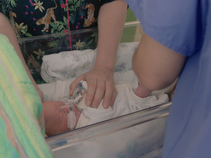 Parent touching their baby who is asleep in a cot