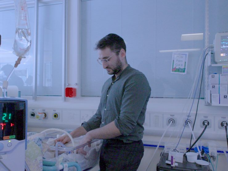 Parent touching their sleeping baby in a hospital room.