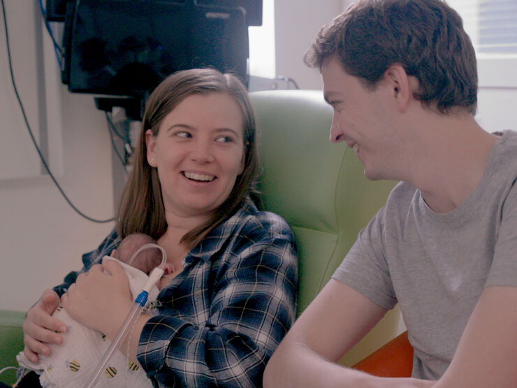 Two parents looking at each other and laughing while their baby rests on the mother's chest
