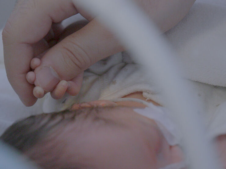 Baby laying down holding onto their parent's thumb.
