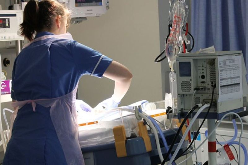 Nurse with her back to camera looking after a baby in a cot, surrounded by lots of medical equipment