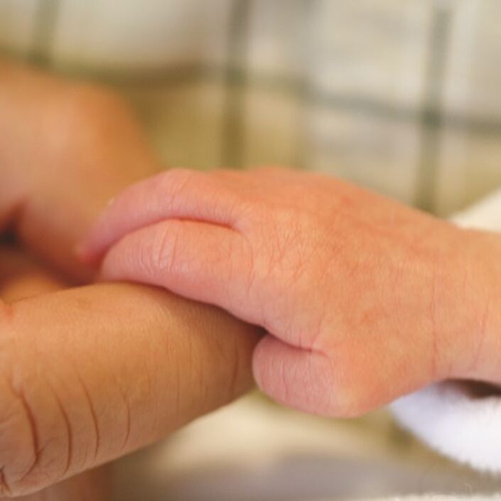 A tiny baby hand grasping onto its parent's index finger.