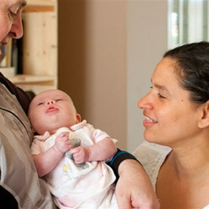 Dad holding a baby smiling looking down at baby with mum alongside also looking at the baby