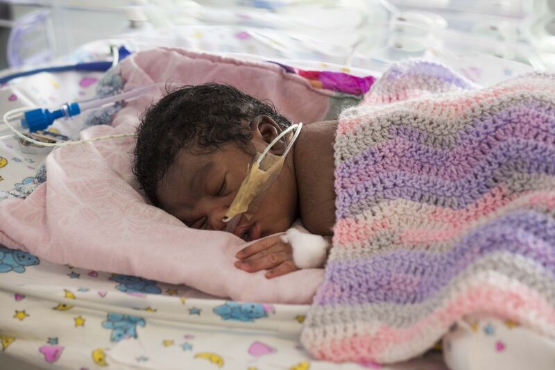 Baby covered in multi-coloured wool blanket while being tube fed